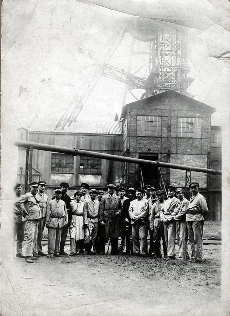 Grupa pracowników kopalni stoi przed zakładem pracy.