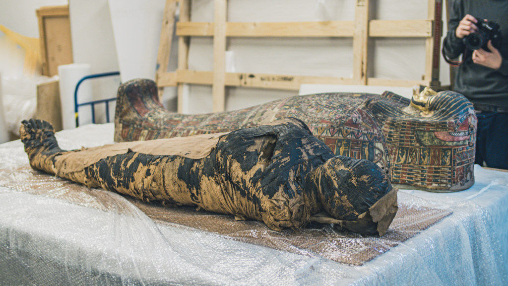 Ozdobny sarkofag i mumia leżą na stole.