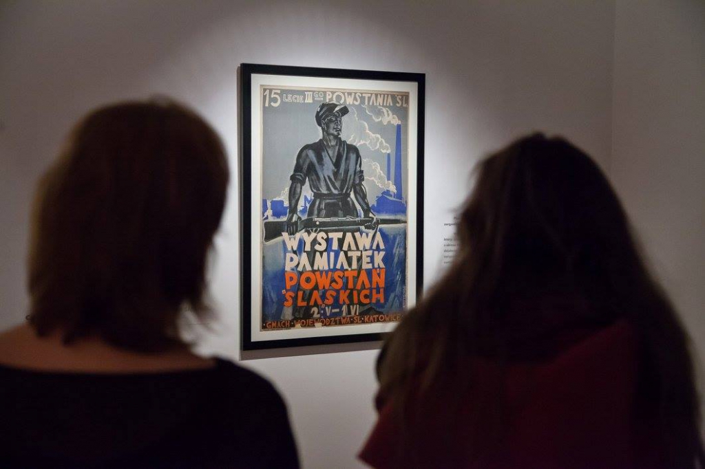 Dwie kobiety patrzą na plakat dotyczący rocznicy III-go powstania śląskiego.