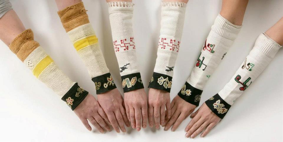 sześć rąk wystawionych do przodu, na przedramionach ozdobne rękawy charakterystyczne dla kultury albańskiej.