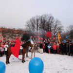 Dwóch mężczyzn na koniach, w strojach królów, otoczonych przez tłum ludzi.