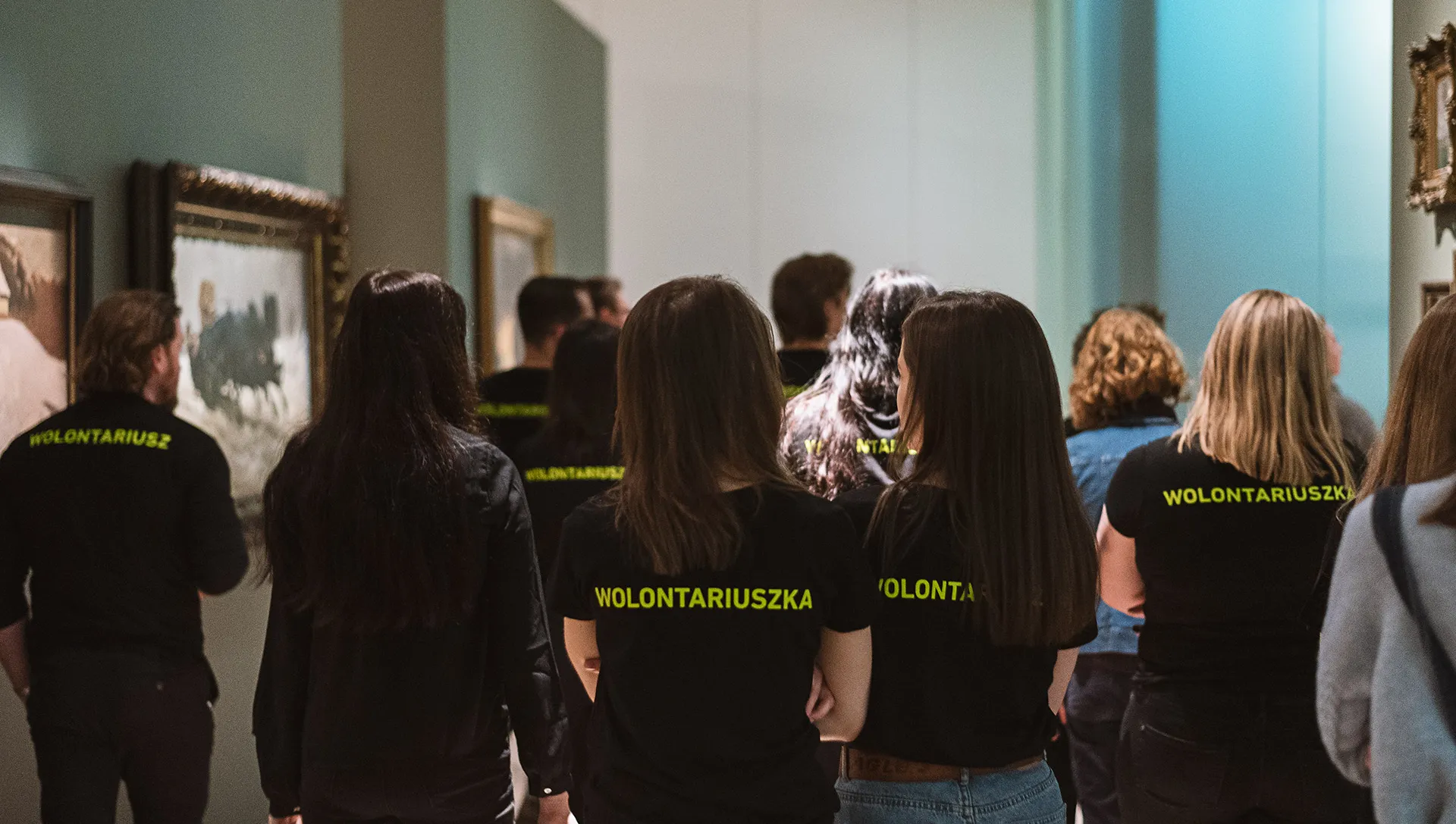 Grupa ludzi w czarnych koszulkach z neonowym napisem wolontariusz lub wolontariuszka.