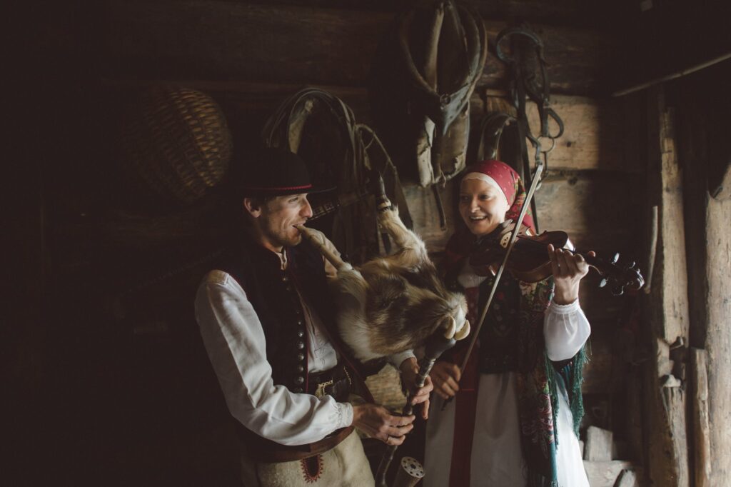 Mężczyzna i kobieta, w strojach góralskich, grają na instrumentach muzycznych.