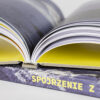 Grzbiet książki z napisem „Spojrzenie z góry”, otwarte strony ukazujące żółte wnętrze okładki.