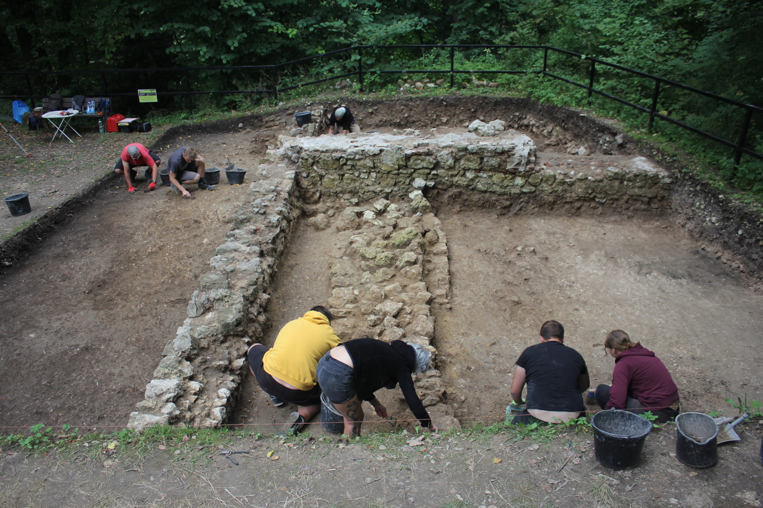 stanowisko archeologiczne, grupa ludzi wykonująca prace, klęczą pochyleni nad ziemią