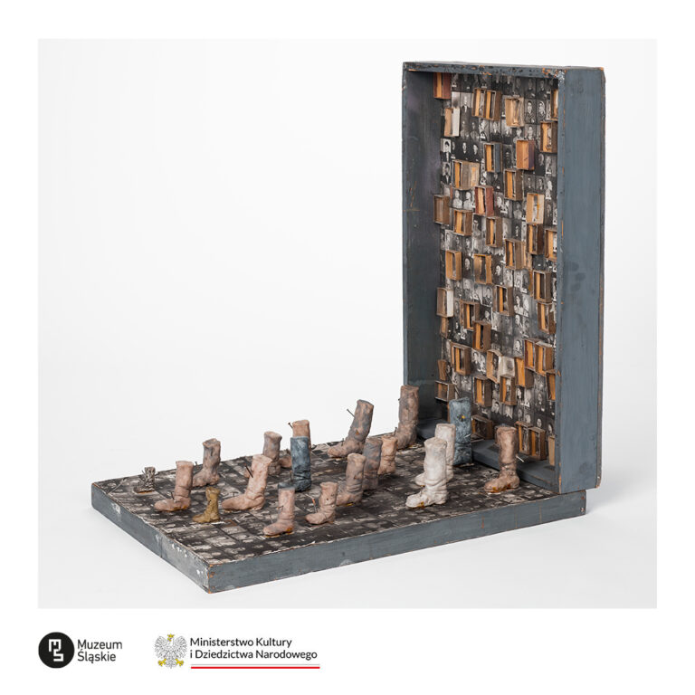 Asamblaż Józefa Szajny przedstawiający szachownicę z pionami w formie uciętych nóg/butów. Pionowa ścianka obiektu wypełniona jest rzędami portretów obozowych i małymi pudełkami. U dołu logotypy Muzeum Śląskiego oraz Ministerstwa Kultury i Dziedzictwa Narodowego.